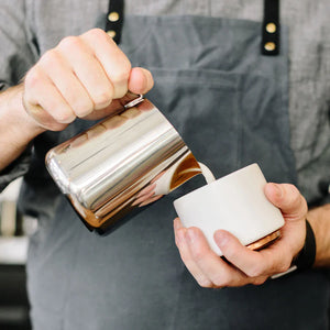 Barista nalévá mléko z leštěné konvičky z nerezové oceli, součást Espresso příslušenství a mléčné konvičky, vše o kávě.