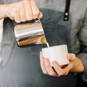 Barista nalévá mléko z leštěné konvičky z nerezové oceli, součást Espresso příslušenství a mléčné konvičky, vše o kávě.