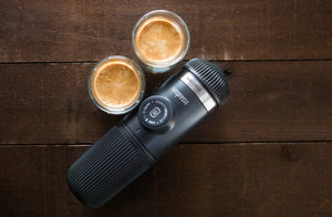 Přenosný espressovač se dvěma šálky espressa na dřevěném povrchu, z přenosných kávovarů a baristického vybavení